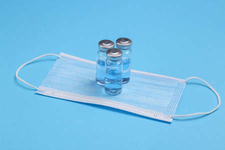 Glass vaccine bottles with medical mask on blue background