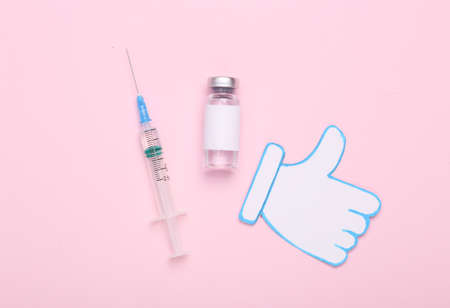 Approved vaccine. Vaccine bottle with blank label for the brand and syringe, thumbs up icon on pink background. Covid 19 pandemic, vaccinationの写真素材