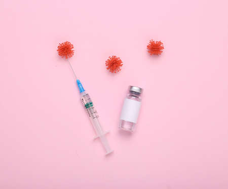 Vaccination, covid 19 treatment. Vaccine bottle with blank label for brand, virus molecules and syringe on pink background. top view. flat layの写真素材
