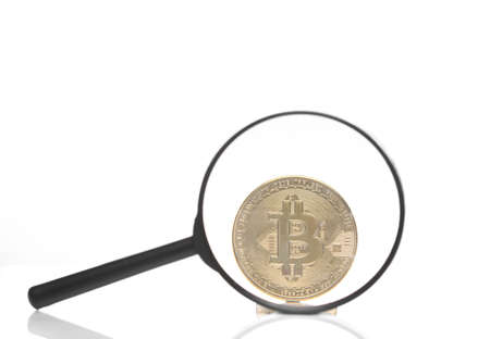 Golden bitcoin coin through a magnifying glass isolated on white background with reflectionの写真素材
