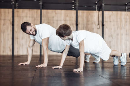 The concept of a healthy family. Father coach doing push-ups with his son in the gym. Fitness, sports, active lifestyleの写真素材