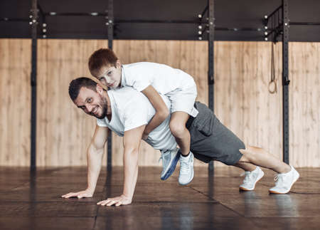 The concept of a healthy family. Father coach doing push-ups with his son in the gym. Fitness, sports, active lifestyleの写真素材