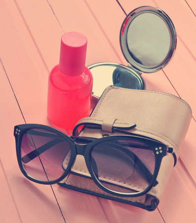 Women's accessories on a pink wooden background. Mirror, sunglasses, purse, perfume bottle.の写真素材