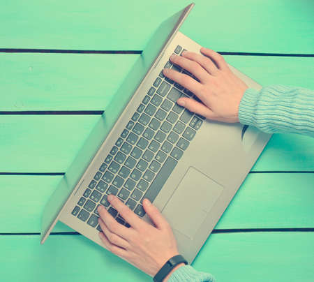 Hands are typing on the laptop keyboard on a blue wooden table. The concept of freelancing, work on...