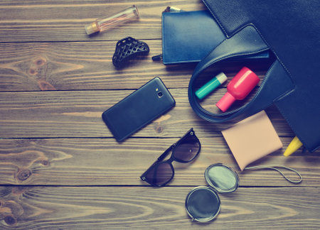 What's in the women's bag? Women's trendy accessories on a wooden background. Smartphone, perfume bottle, power bank, mirror, sunglasses, lipstick. top view.の写真素材