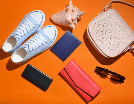 Women's trendy travel accessories and technology gadgets on orange surface. Sneakers, passport, purse, glasses, smartphone, power bank, shell. top view. flat lay.の写真素材