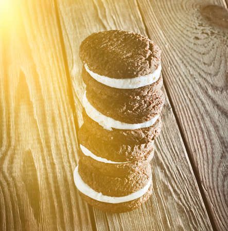 Chocolate cookies with milky cream filling on a rustic wooden table.