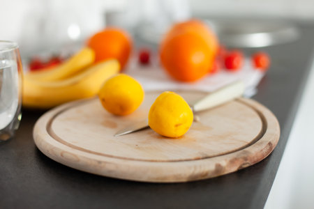 Sliced lemon on wooden board with knife and fruits on kitchen countertopの写真素材