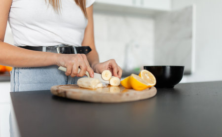 Young woman cuts fruit for salad in a modern kitchen. healthy food conceptの写真素材