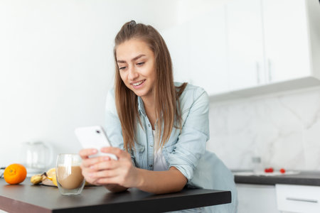 Lovely young woman using smartphone in the kitchenの写真素材