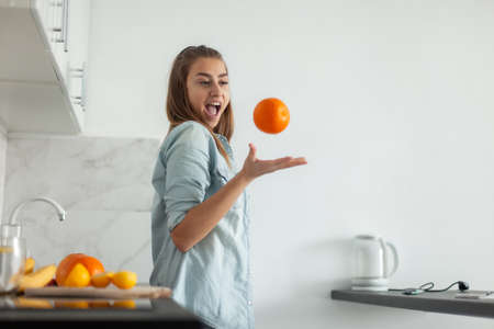Emotional woman tossing an orange in the kitchenの写真素材