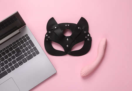 Online erotic chat. BDSM leather cat mask with vibrator and laptop on a pink background. Top view. flat layの写真素材