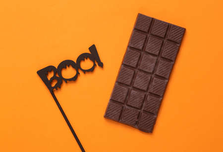 Halloween minimal still life. The word boo on a stick with a bar of chocolate on an orange...