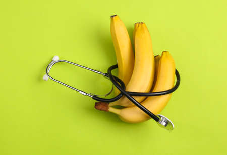 Healthy food concept. Bananas wrapped with a stethoscope on green backgroundの写真素材