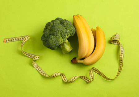Broccoli and banana with measuring tape on green background. Weight loss concept. Top viewの写真素材