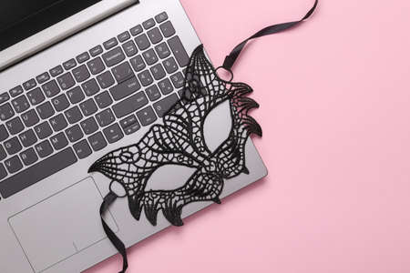 Online erotic chat. Lace cat mask with laptop on a pink background. Top view. flat layの写真素材