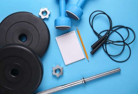 Healthy lifestyle, creation of a training program for bodybuilding and fitness. Blank notepad with dumbbells, barbell and jump rope on blue backgroundの写真素材