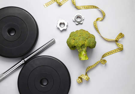 Fitness, weight loss concept. Barbell with measuring tape and broccoli isolated on white background. Top viewの写真素材