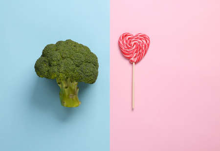 Healthy versus junk food. Broccoli and lollipop on a blue-pink background. Weight loss, diet conceptの写真素材