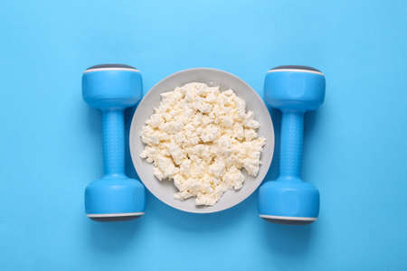 Healthy lifestyle concept. Dumbbells with a plate of cottage cheese on a blue background. Fitness...