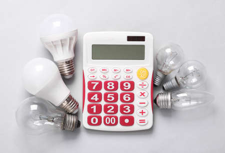 Calculation of the cost of electricity. Calculator and different light bulbs on gray background. Top...