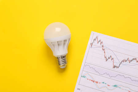 Led light bulb with chart on yellow background. Power consumption efficiency analysisの写真素材
