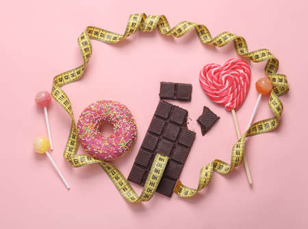 Weight loss, diet concept. Lollipops, donut and chocolate bar with measuring tape on pink backgroundの写真素材