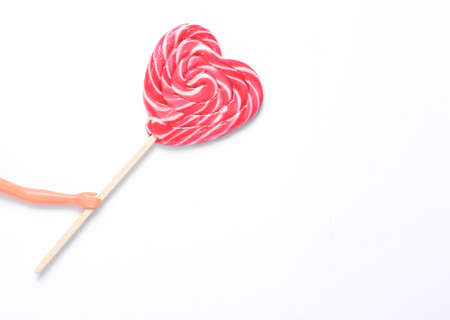 The doll's hand holds a heart-shaped lollipop on white background. Minimal still lifeの写真素材