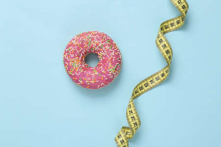 Diet concept. High calorie donut with measuring tape on blue backgroundの写真素材