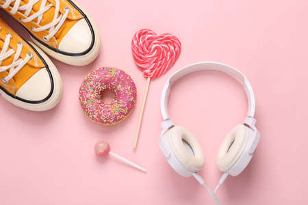 Headphones with sneakers and sweets on a pink background. Minimal youth still life. Top viewの写真素材