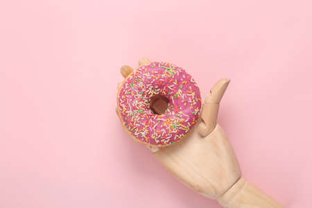 Wooden hand holding donut on pink backgroundの写真素材
