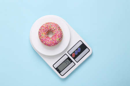diet concept. High calorie donut on scales, blue backgroundの写真素材