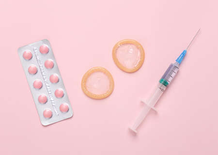 contraceptives. Condoms with birth control pills and a syringe on a pink background.