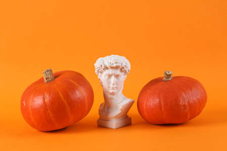 Minimal halloween still life. David bust with pumpkins on orange background