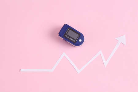 Electronic pulse oximeter with statistics growth arrow on a pink background. Covid-19 disease...