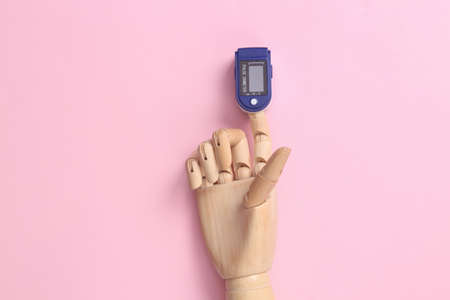 Wooden hand with a clip-on pulse oximeter on a finger on pink background