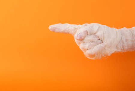 A mummy's hand wrapped in white bandages points with his index finger to the space for text on an orange background. Happy Halloween. Trick or Treatの写真素材