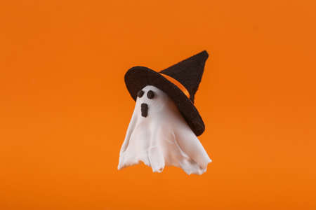 Handmade plasticine ghost with witch hat on orange background. Halloween concept. Trick or Treat