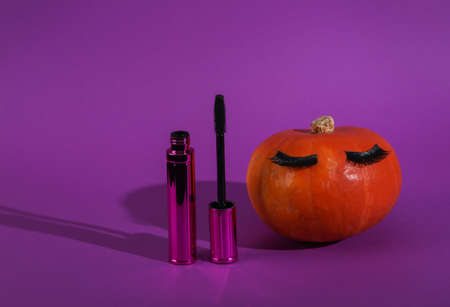 Beauty minimal still life. Pumpkin with false eyelashes and mascara on a purple backgroundの写真素材