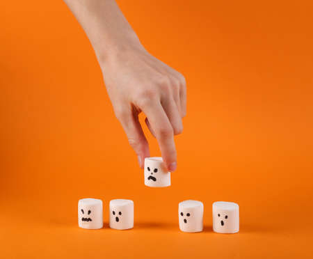Hand takes halloween marshmallow ghost on orange background.の写真素材