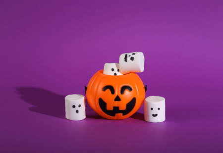 Halloween still life. Jack o'lantern bucket for candies and marshmallows with faces on a bright purple background. Trick or Treatの写真素材