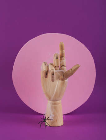 Minimal Halloween still life. Wooden puppet hand with a spider web and a pack on a purple background with a pink circle. fresh ideasの写真素材
