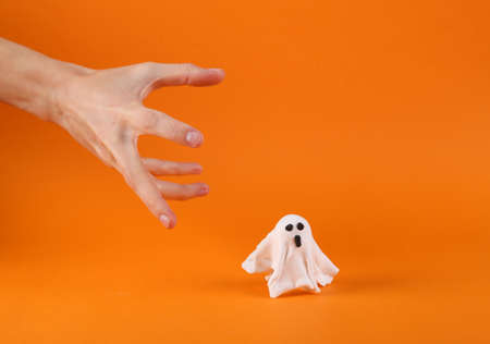 Scary hand with a little ghost on an orange background. Halloween still lifeの写真素材