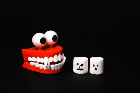 Halloween scene Fanged monster chasing marshmallows with faces on black background.の写真素材