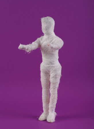 Mummy doll wrapped in bandages on a purple background. Minimal halloween conceptの写真素材