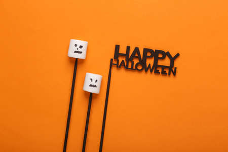 Top view, flat lay halloween layout, marshmallows with faces on sticks and word happy halloween on...