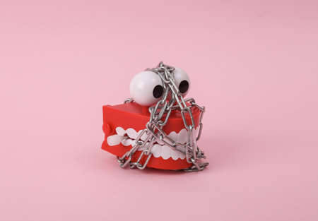 Funny toy clockwork jumping teeth with eyes wrapped with steel chain on pink background. Prohibition...