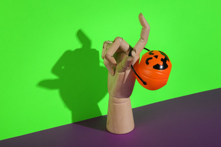 Wooden hand with Halloween candy bucket on green-purple background. Trick or Treatの写真素材