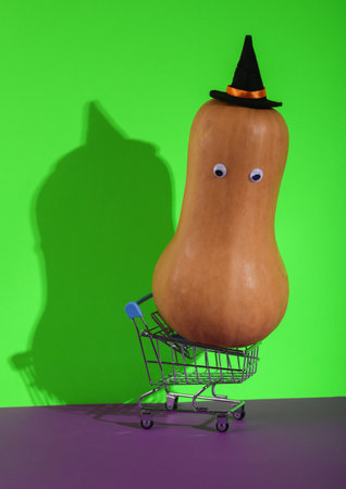 Mini shopping cart with halloween pumpkin on green purple background. creative halloween layoutの写真素材