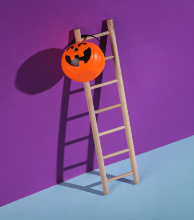 Wooden ladder with Halloween candy bucket on a purple background. Minimal halloween layout.の写真素材